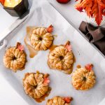 These Apple Cinnamon Pastry Donuts are filled with fresh apple slices, surrounded by puff pastry, covered in cinnamon sugar, drizzled with caramel sauce, and topped with a cinnamon stick and edible maple leaf.