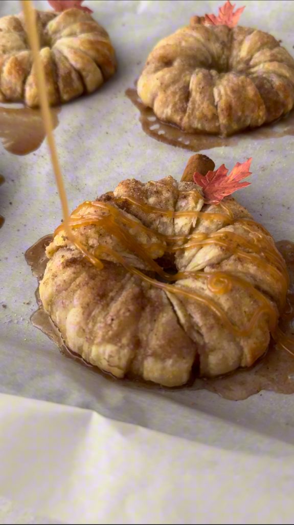 These Apple Cinnamon Pastry Donuts are filled with fresh apple slices, surrounded by puff pastry, covered in cinnamon sugar, drizzled with caramel sauce, and topped with a cinnamon stick and edible maple leaf.
