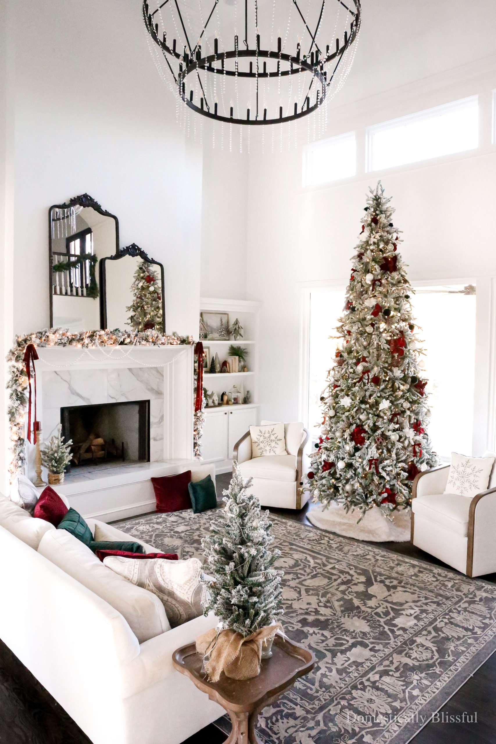 Cozy traditional Christmas Living Room Decor with a 12-foot flocked Christmas tree, flocked garland, and flocked wreaths, with deep red and forest green accents.