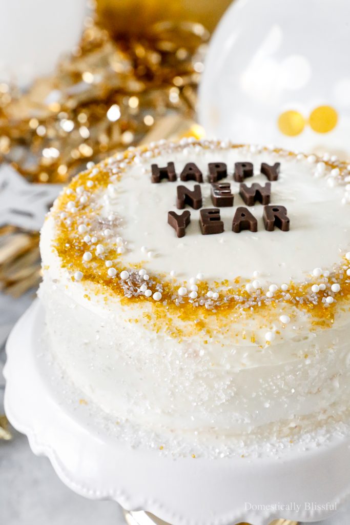 A quick and easy DIY Happy New Year's Eve Cake using a store-bought cake and redecorating it with gold, silver, and white sprinkles and chocolate letters.