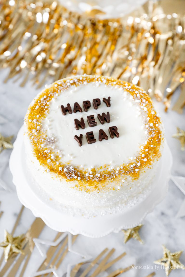 A quick and easy DIY Happy New Year's Eve Cake using a store-bought cake and redecorating it with gold, silver, and white sprinkles and chocolate letters.