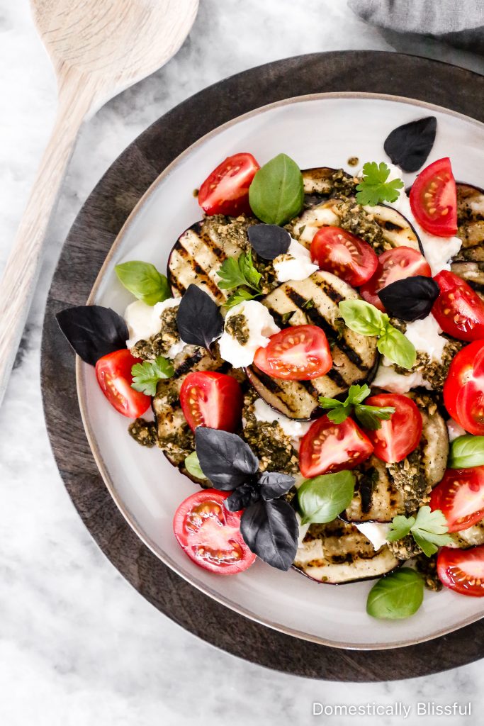 This Grilled Eggplant Salad is marinated, grilled, and topped with whipped ricotta, pesto, quartered tomatoes, and fresh herbs.