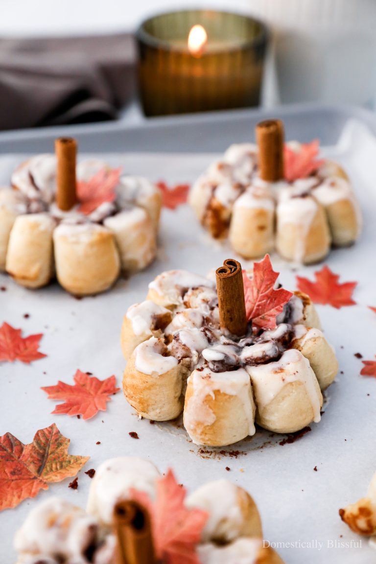 These Pumpkin Cinnamon Rolls are made with store-bought cinnamon roll dough and formed into the shape of a pumpkin topped with a cinnamon stick and an edible leaf.