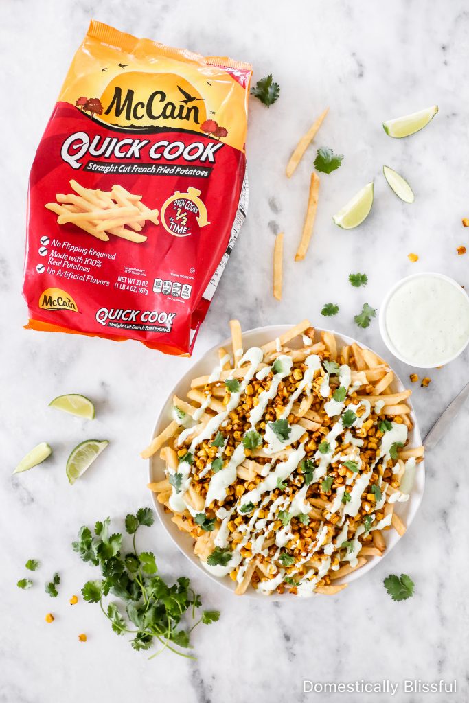 These Mexican Street Corn Fries are super easy to make with a base of crispy fries and melted cheese, topped with roasted corn, drizzled with cilantro cream sauce, and a squeeze of lime.